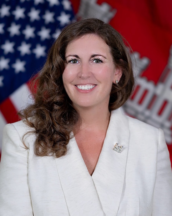 Portrait of a Caucasian female in a white business jacket with the American and U.S. Army Corps of Engineers flag in the background.