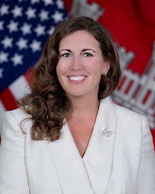 Portrait of a Caucasian female in a white business jacket with the American and U.S. Army Corps of Engineers flag in the background.