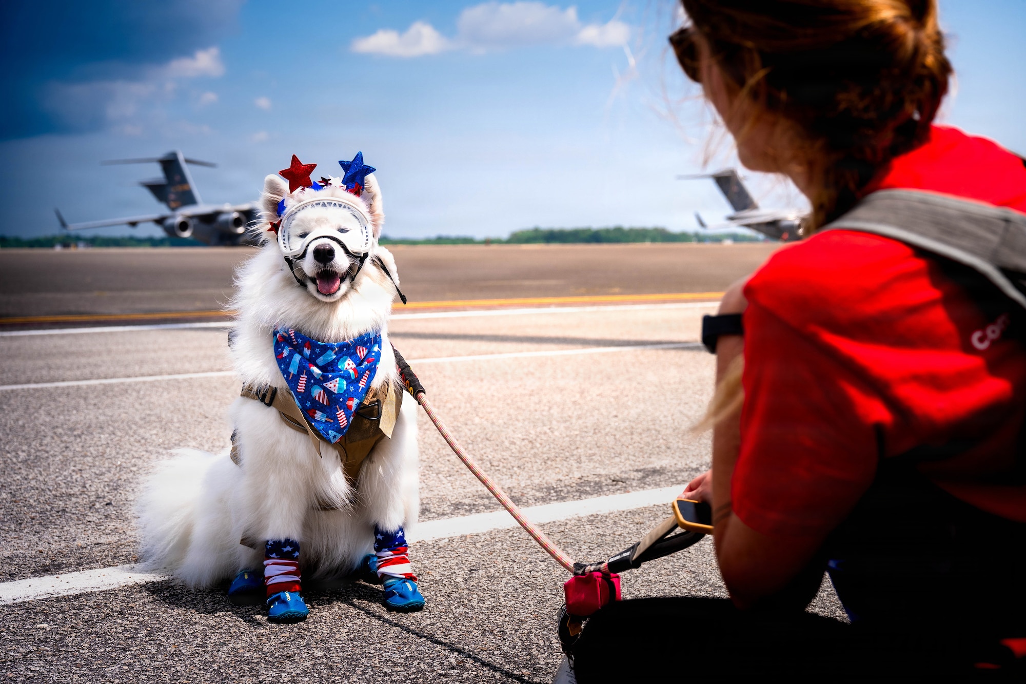 A photo of a woman and dog sitting on the flightline.