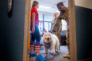 A photo of three people and a dog standing in a room together.