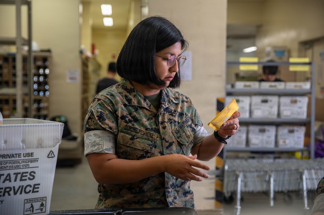 U.S. Marine Corps Cpl. Victoria Coronelpesantez, a postal clerk with Headquarters and Headquarters Squadron (H&HS), Marine Corps Air Station Iwakuni, and a native of Queens, New York, inspects a package during a postal field exercise at MCAS Iwakuni, Japan, June 29, 2026. MCAS Iwakuni post office conducted a postal field exercise to practice operating expeditionary field post offices. (U.S. Marine Corps photo by Lance Cpl. Kenneth Garcia)