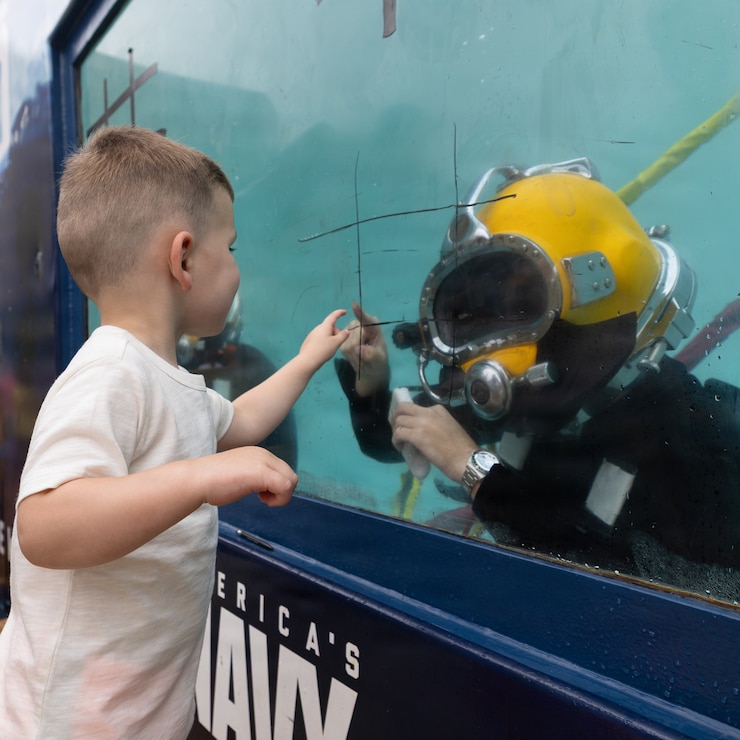Petty Officer 2nd Class Luke Malkowski, a navy diver assigned to Explosive Ordnance Demolition Mobile Unit 12, interacts with a child as part of an interactive exhibit in Baltimore Inner Harbor