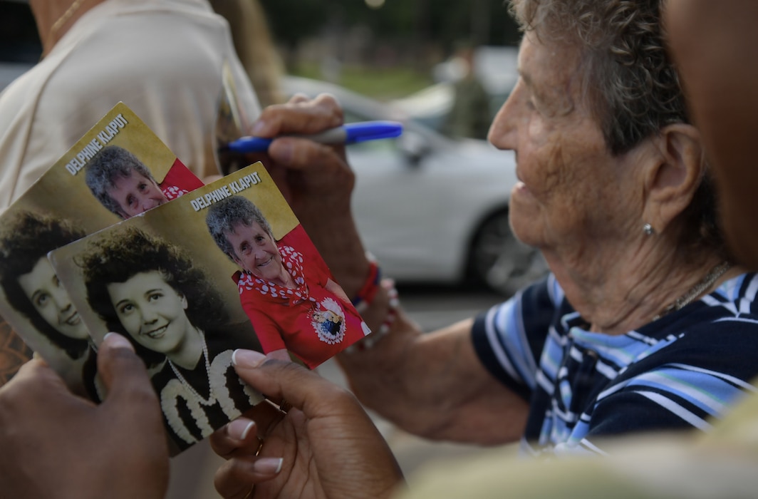 An elderly woman autographs a post card.