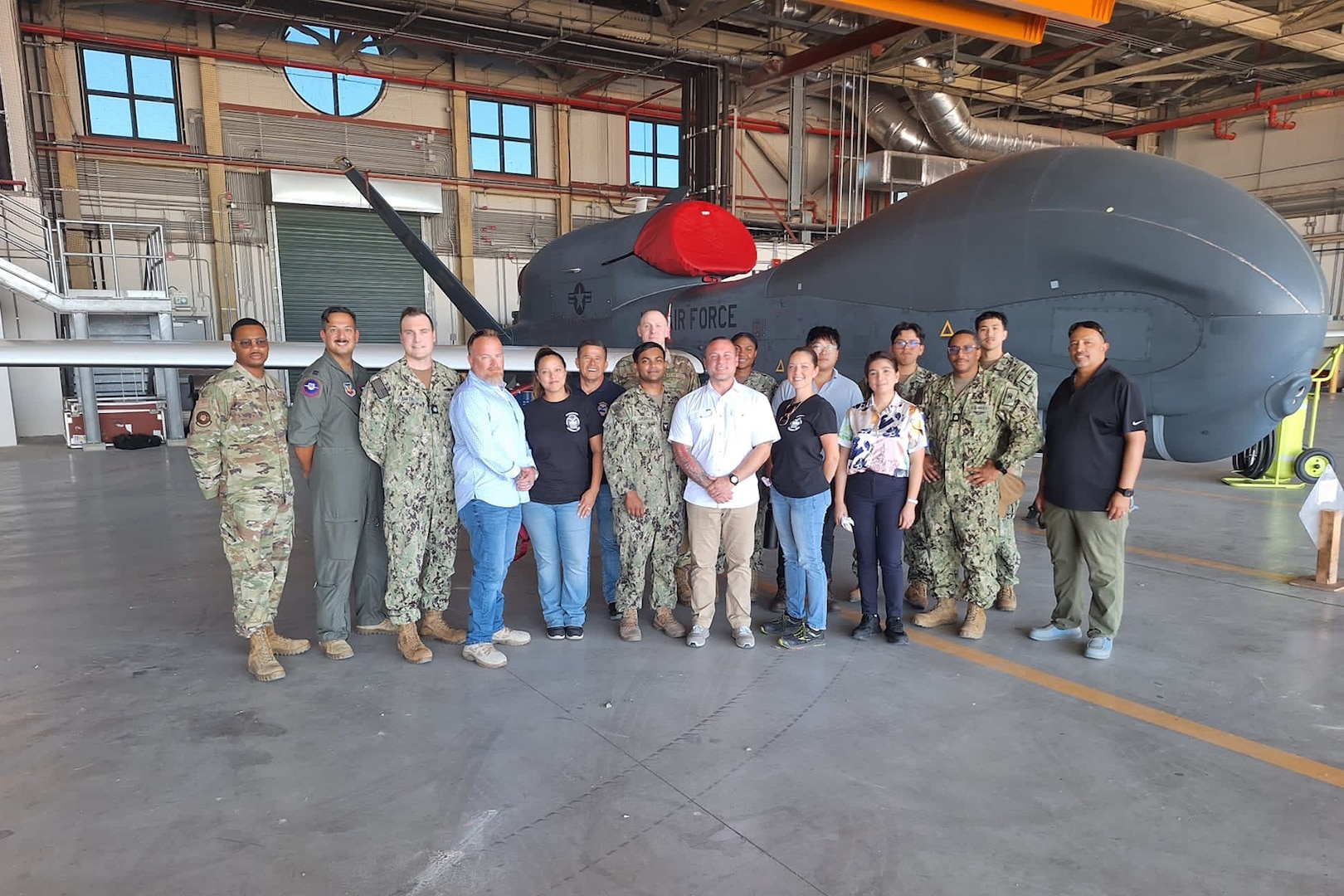 A group of people, some wearing military uniforms, stand in front of an aircraft in a hangar.