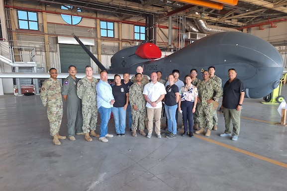 A group of people, some wearing military uniforms, stand in front of an aircraft in a hangar.