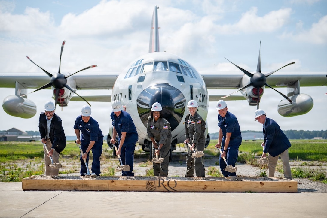 Coast Guard breaks ground on new runway with a Coast Guard HC-130J airplane in the background.