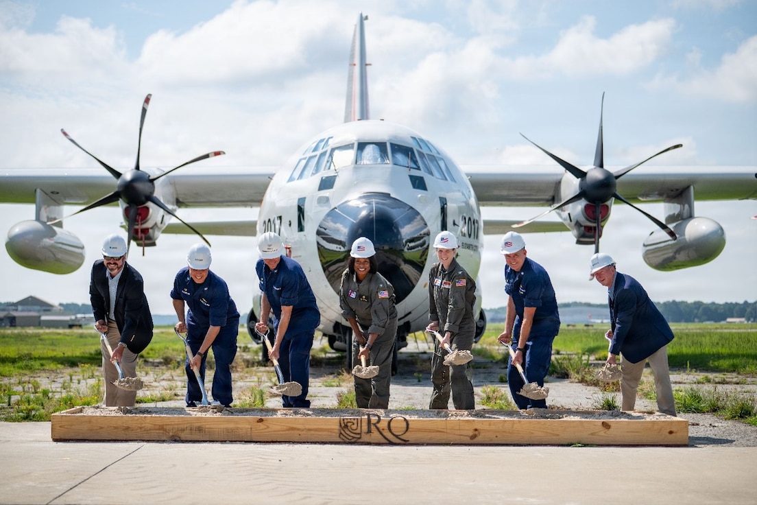 Coast Guard breaks ground on new runway with a Coast Guard HC-130J airplane in the background.