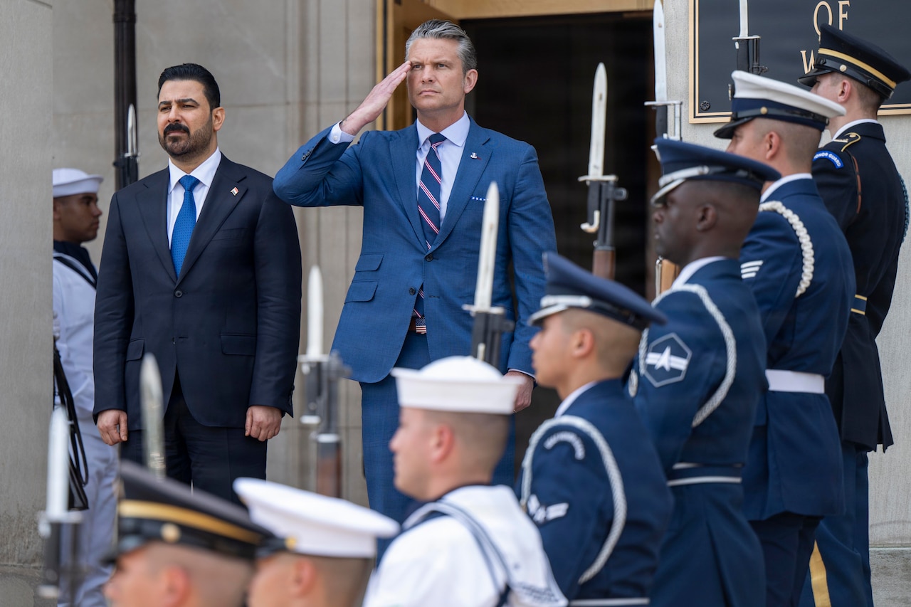 A man in a suit renders a salute as another man in similar attire stands next to him outside of a building.