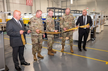 Five men cutting a golden ceremonial ribbon with large gold scissors. Three center men are in Army Uniform, both men on their sides are wearing suits.