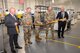 Five men cutting a golden ceremonial ribbon with large gold scissors. Three center men are in Army Uniform, both men on their sides are wearing suits.