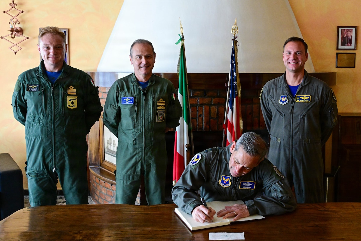 A man signs a document while other men watch.