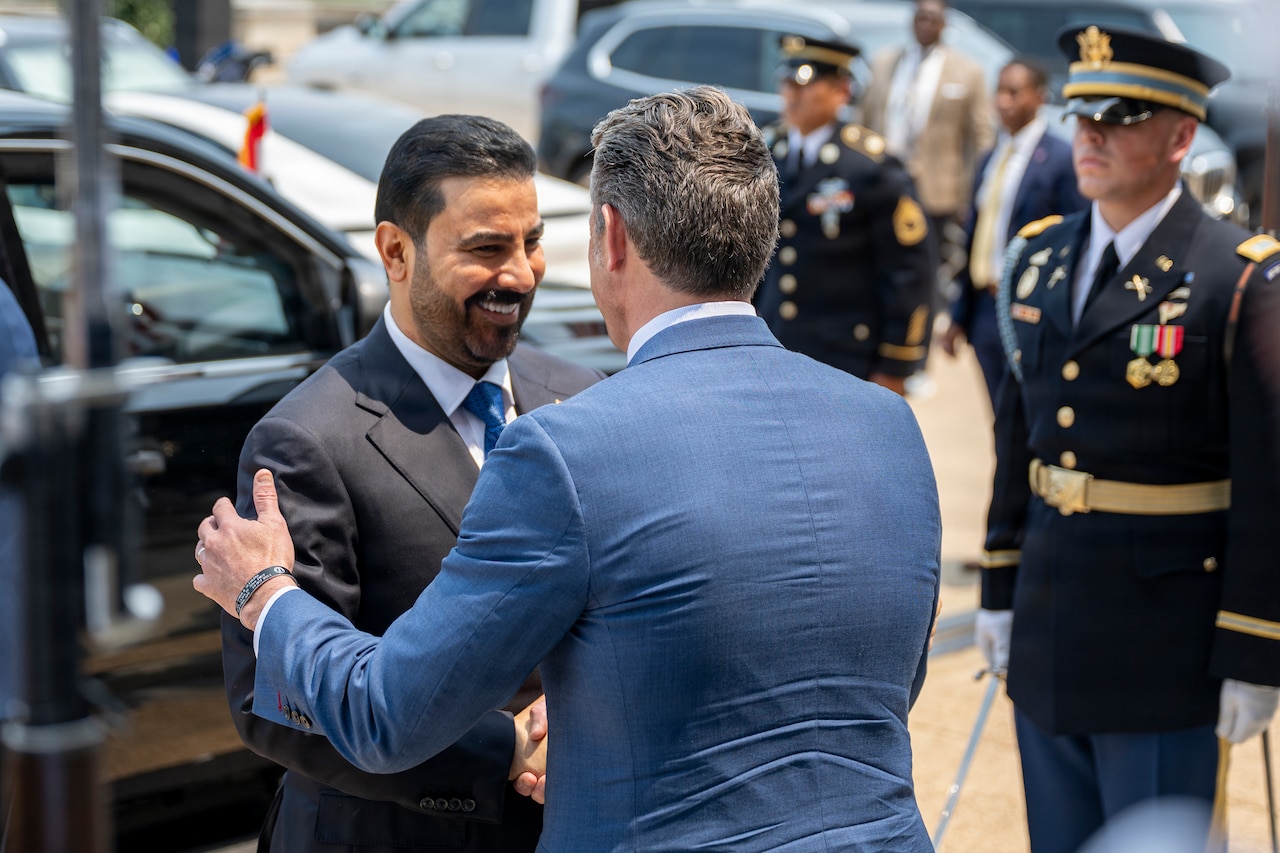 Two men in suits shake hands outside of a building.