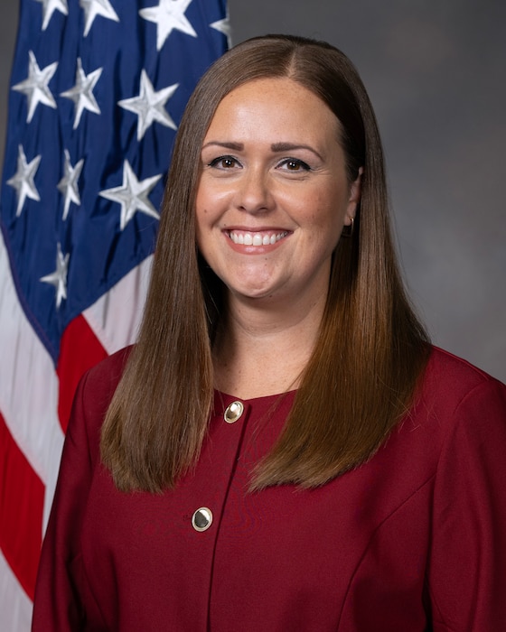 Headshot of woman in red jacket in front of American flag.