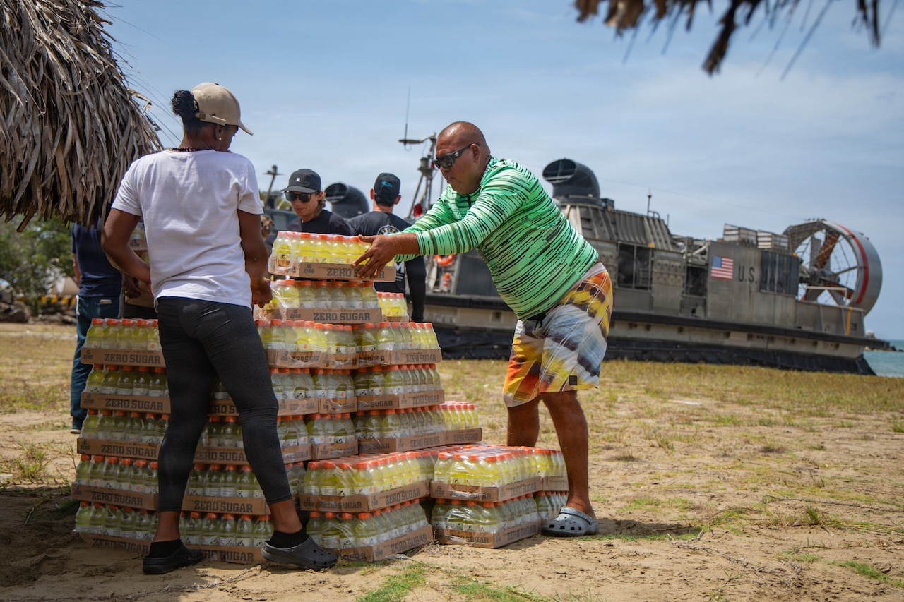Two people in casual civilian clothing remove cases of beverages from a pallet