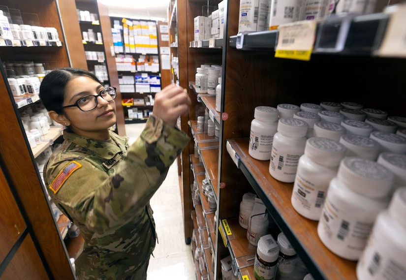 Service member reaches toward shelves in a military pharmacy