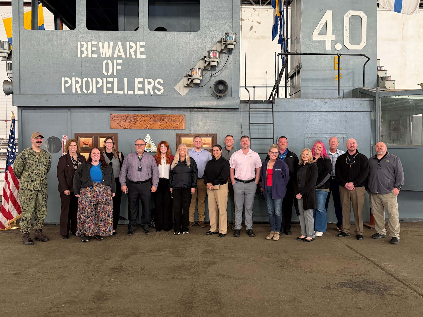 A large group of people stand on a mock-up of a Navy aircraft carrier deck.