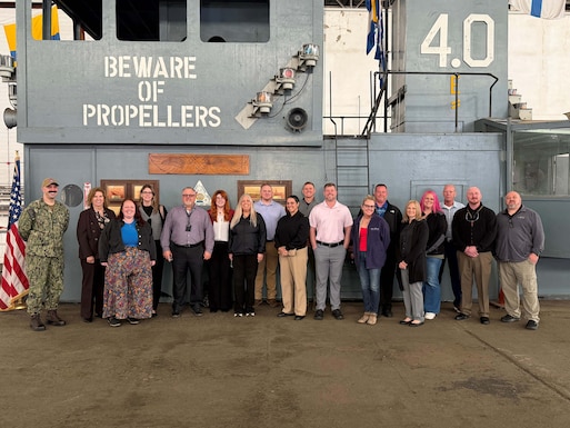 A large group of people stand on a mock-up of a Navy aircraft carrier deck.
