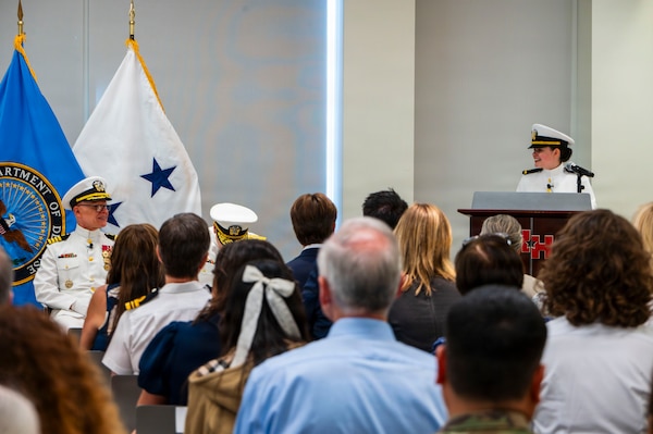 (260710-N-AJ782-1209) FALLS CHURCH, Va. From left to right, U.S. Navy Capt. Lonnie S. Hosea, Bureau of Medicine and Surgery senior health policy advisor, smiles at his daughter, Ensign Jenna Hosea Baker, a nurse assigned to Walter Reed National Military Medical Center, as she delivers remarks as part of a joint ceremony featuring the retirement of Hosea and the commissioning of Baker at Defense Health Headquarters in Falls Church, Virginia, July 10, 2026. The ceremony highlighted a continuing legacy of service for Navy Medicine as Hosea closed out a 30-year career and Baker took her first steps into the Nurse Corps. (U.S. Navy photo by Kevin Ray J. Salvador)