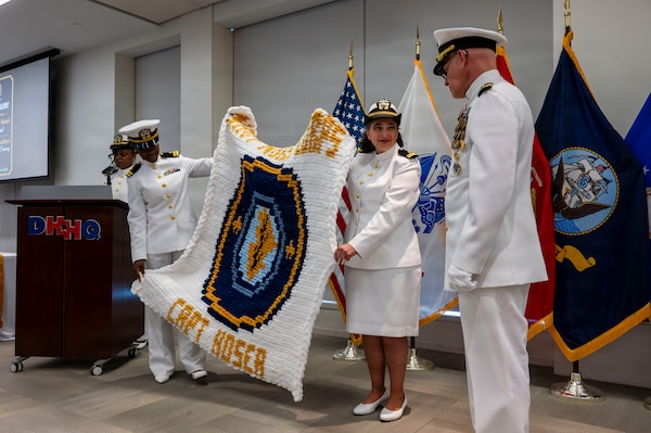 (260710-N-AJ782-1361) FALLS CHURCH, Va. U.S. Navy Capt. Lonnie S. Hosea, right, Bureau of Medicine and Surgery senior health policy advisor, receives a gift as part of a joint retirement and commissioning ceremony at Defense Health Headquarters in Falls Church, Virginia, July 10, 2026. Hosea and his daughter, Ensign Jenna Hosea Baker, who is a nurse assigned to Walter Reed National Military Medical Center, highlighted a continuing legacy of service for Navy Medicine as Hosea closed out a 30-year career and Baker took her first steps into the Nurse Corps. (U.S. Navy photo by Kevin Ray J. Salvador)