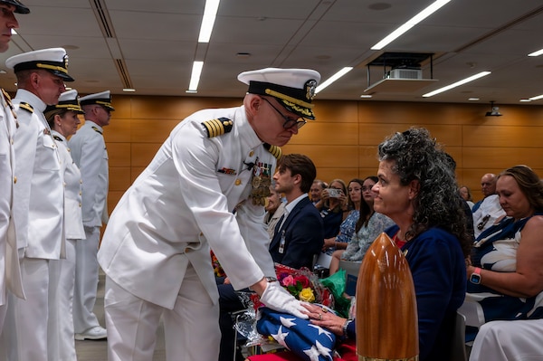 (260710-N-AJ782-1547) FALLS CHURCH, Va. From left to right, U.S. Navy Capt. Lonnie S. Hosea, Bureau of Medicine and Surgery senior health policy advisor, presents the flag to his wife, Deanna McAlister Hosea, as part of a joint retirement and commissioning ceremony at Defense Health Headquarters in Falls Church, Virginia, July 10, 2026. Hosea and his daughter, Ensign Jenna Hosea Baker, who is a nurse assigned to Walter Reed National Military Medical Center, highlighted a continuing legacy of service for Navy Medicine as Hosea closed out a 30-year career and Baker took her first steps into the Nurse Corps. (U.S. Navy photo by Kevin Ray J. Salvador)