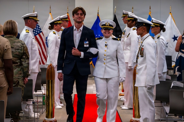 (260710-N-AJ782-1644) FALLS CHURCH, Va. From right to left,  Ensign Jenna Hosea Baker, a nurse assigned to Walter Reed National Military Medical Center, is piped ashore alongside her husband, Andrew Baker, during a joint ceremony featuring the retirement of her father, Capt. Lonnie S. Hosea, U.S. Navy Bureau of Medicine and Surgery senior health policy advisor, and her commissioning at Defense Health Headquarters in Falls Church, Virginia, July 10, 2026. The ceremony highlighted a continuing legacy of service for Navy Medicine as Hosea closed out a 30-year career and Baker took her first steps into the Nurse Corps. (U.S. Navy photo by Kevin Ray J. Salvador)