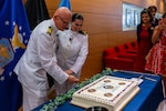 (260710-N-AJ782-1654) FALLS CHURCH, Va. From left to right, U.S. Navy Capt. Lonnie S. Hosea, Bureau of Medicine and Surgery senior health policy advisor, and his daughter, Ensign Jenna Hosea Baker, a nurse assigned to Walter Reed National Military Medical Center, cut his retirement cake as part of a joint ceremony featuring the retirement of Hosea and the commissioning of Baker at Defense Health Headquarters in Falls Church, Virginia, July 10, 2026. The ceremony highlighted a continuing legacy of service for Navy Medicine as Hosea closed out a 30-year career and Baker took her first steps into the Nurse Corps. (U.S. Navy photo by Kevin Ray J. Salvador)