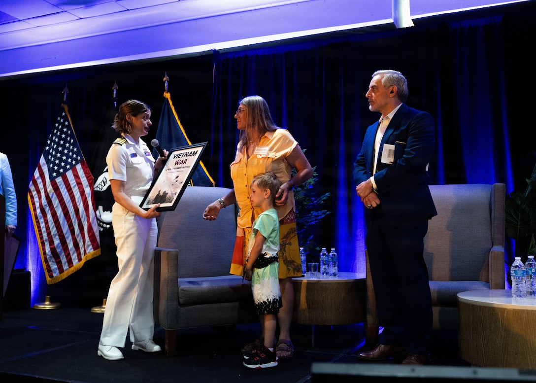 U.S. Navy Capt. Meghan Bodnar, Defense POW/MIA Accounting Agency deputy director of operations, left, presents a plaque to Karen Steadman, Gold Star family member and daughter of U.S. Air Force Capt. James E. Steadman, right