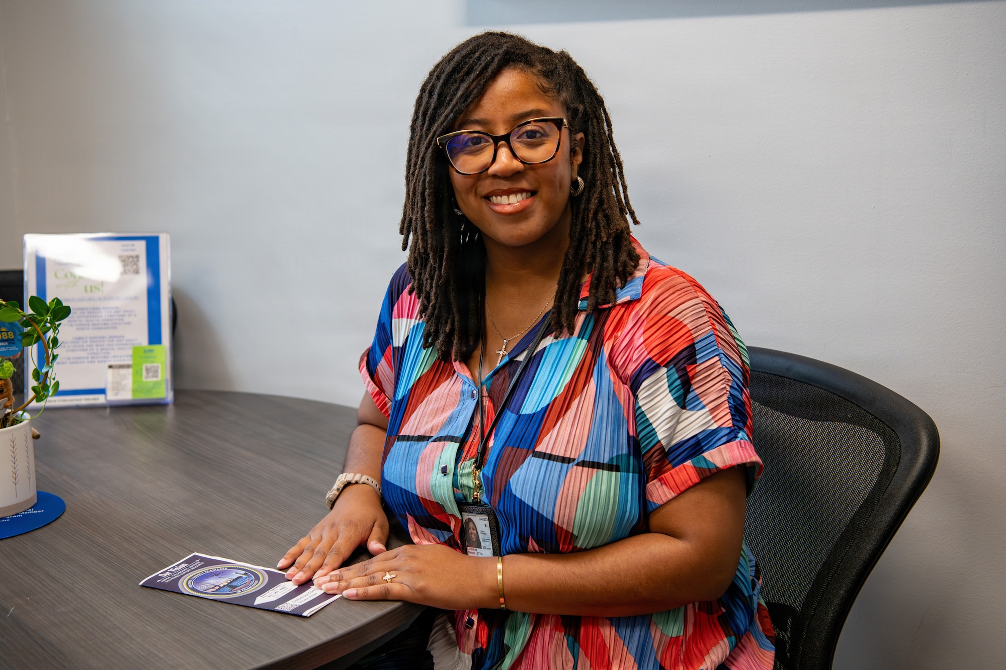 A woman sits and smiles for a portrait while holding a pamphlet in an office.