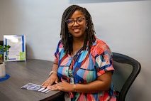 A woman sits and smiles for a portrait while holding a pamphlet in an office.