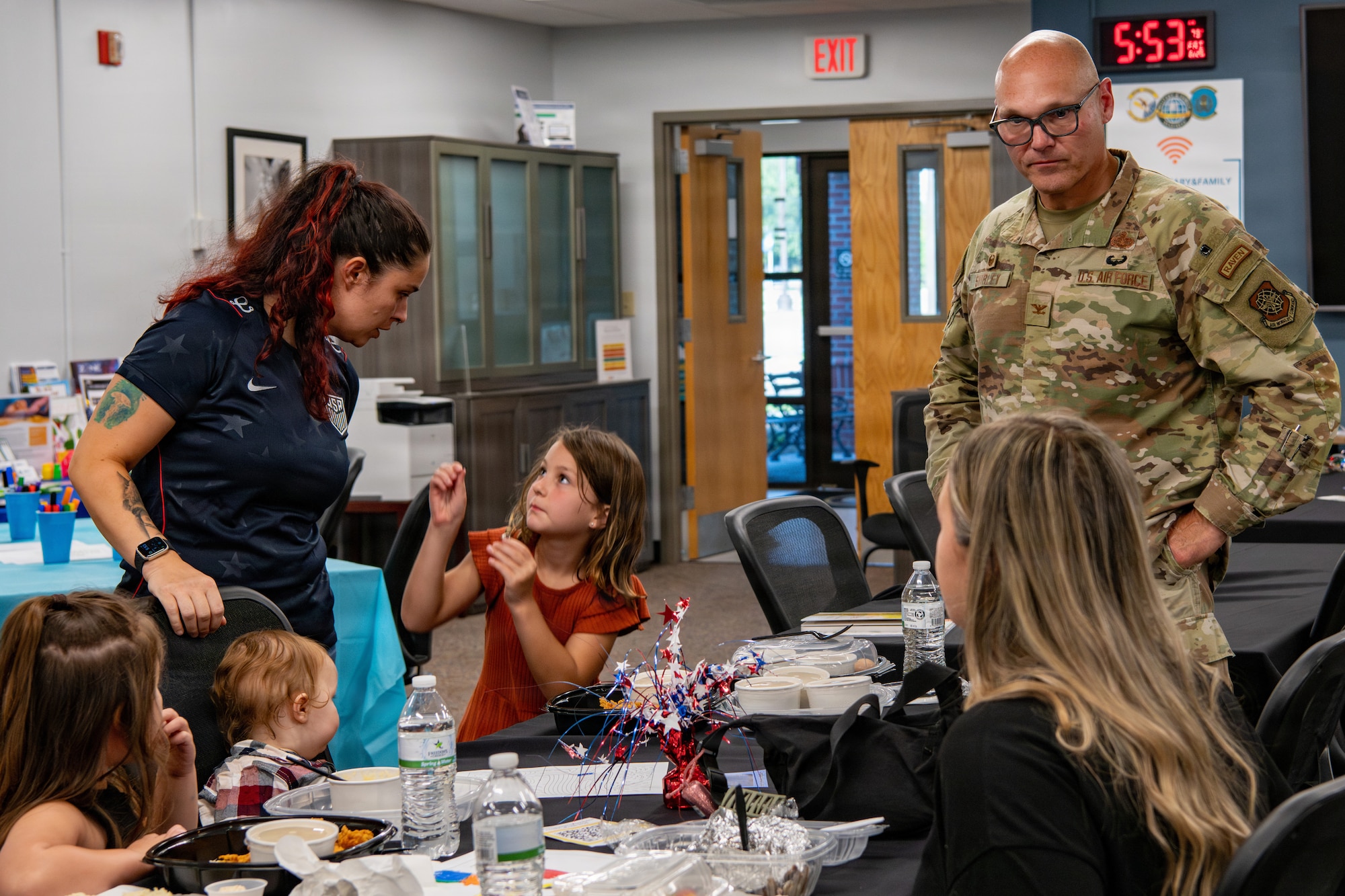 A uniformed service member engages with two women and their children.