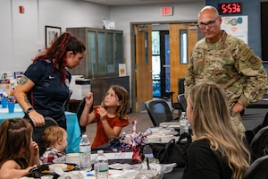 A uniformed service member engages with two women and their children.