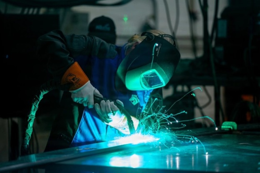 A person wearing a welding mask uses a welding torch on a flat metal surface.