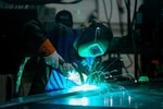 A person wearing a welding mask uses a welding torch on a flat metal surface.