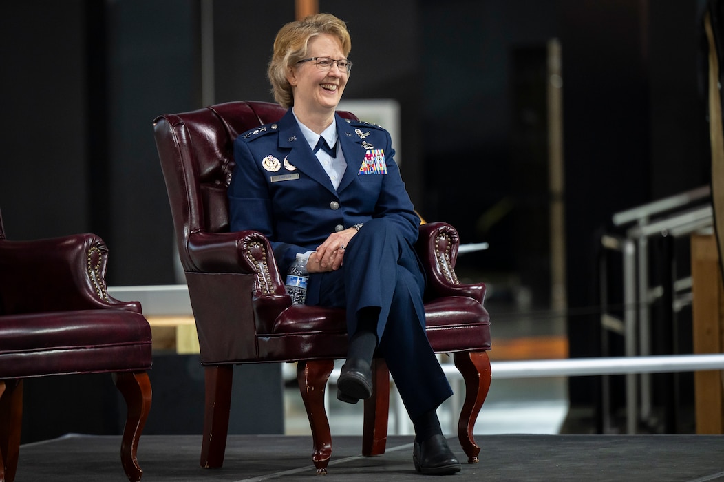Female Air Force officer wearing dress blues sits in chair on stage.