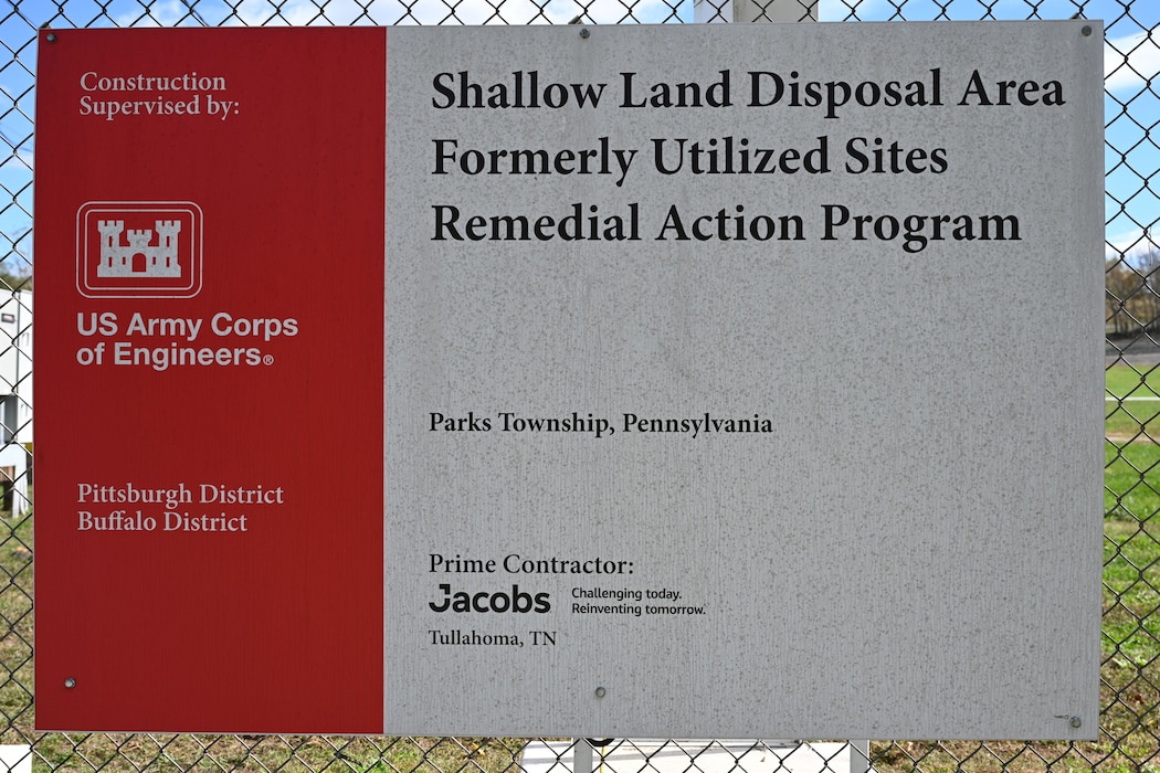 A close-up of a sign on a chain-link fence. The sign reads "Shallow Land Disposal Area Formerly Utilized Sites Remedial Action Program" and lists the US Army Corps of Engineers and prime contractor Jacobs.