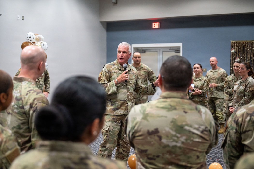 A service member speaks into a microphone in the middle of a crowd.