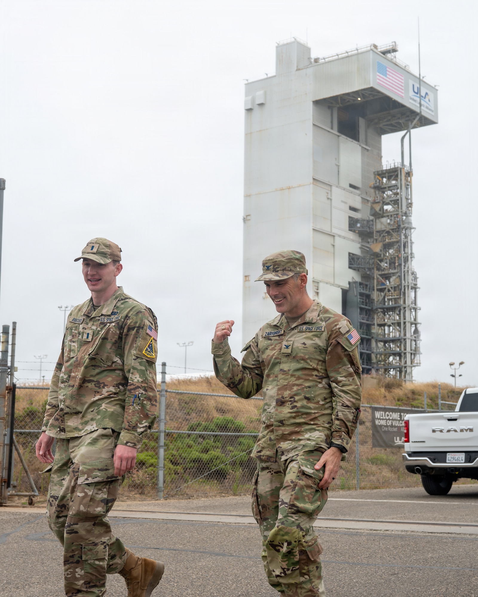 Two military members walk away from a space launch complex.