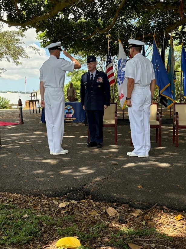One Navy captain salutes an Air Force major general, while another Navy captain looks on.