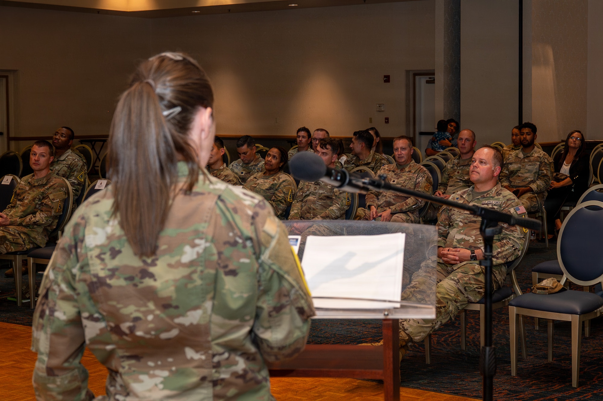 A person stands behind a podium and speaks to a seated crowd