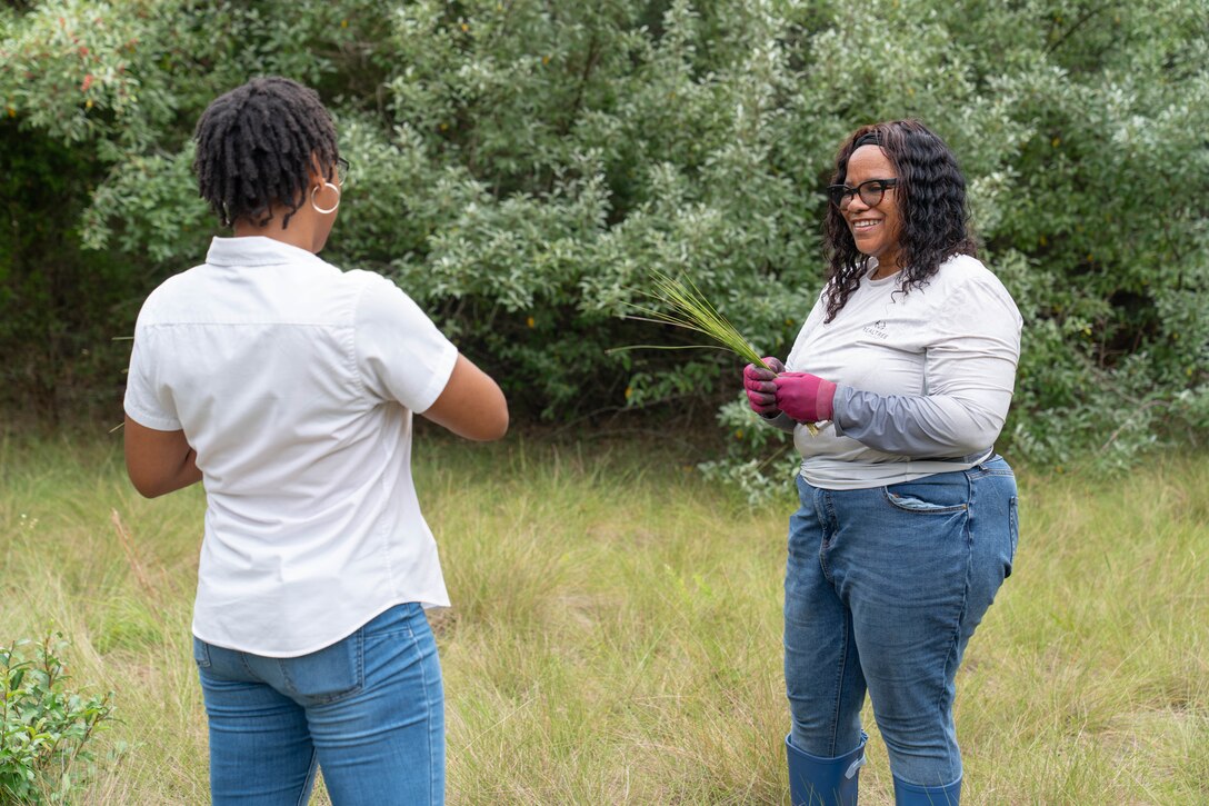 Two people standing across from each other hold and discuss sweetgrass, a native coastal perennial grass prized for its strength and flexibility.