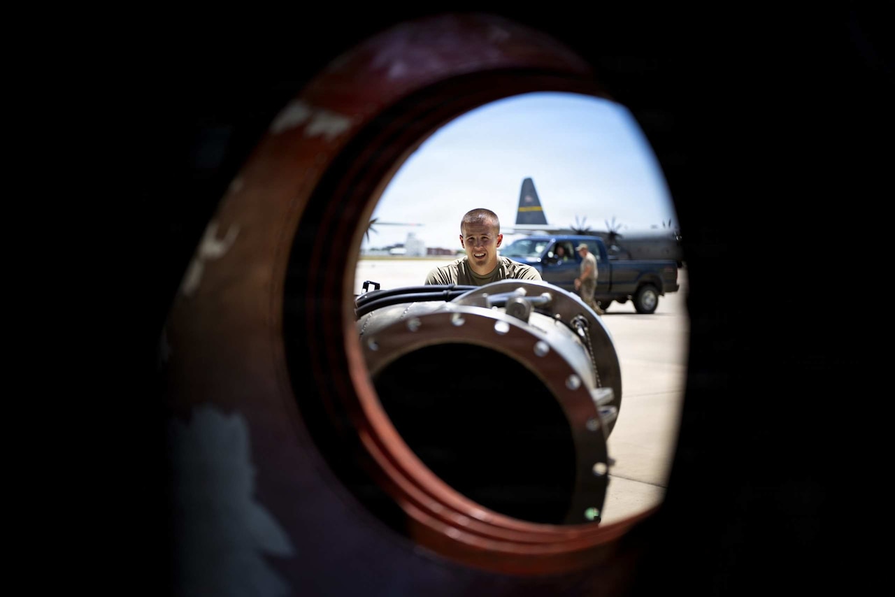 A man pushes a nozzle through the side of a cargo plane to connect a firefighting system.