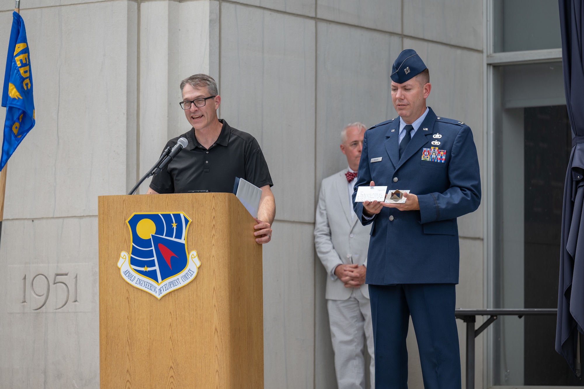 Air Force Test Center Commander and former Arnold Engineering Development Complex commander Maj. Gen. Scott Cain, left, describes the burst disc from testing at AEDC Hypervelocity Wind Tunnel 9 at White Oak, Md., he contributed to the AEDC time capsule unveiled June 27, 2026, during the AEDC 75th anniversary open house celebration at Arnold Air Force Base, Tenn., headquarters of AEDC. Pictured holding the disc is AEDC Executive Officer Capt. Nathan Tedder, right. Also pictured is AEDC Historian Ken Sloat. (U.S. Air Force photo by Keith Thornburgh)