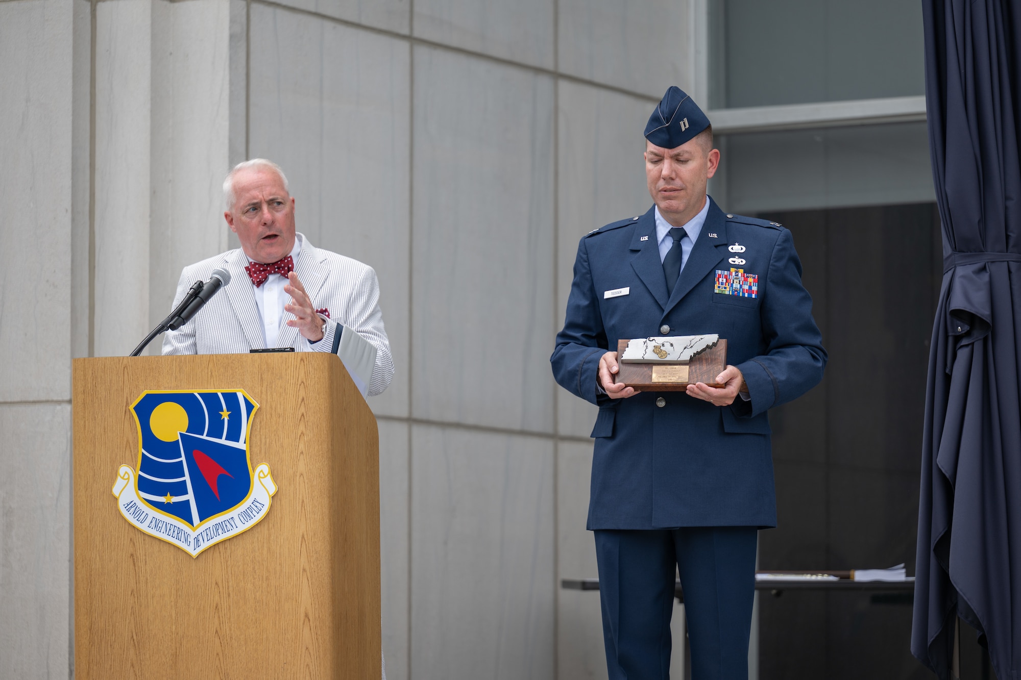 Arnold Engineering Development Complex Historian Ken Sloat, left, describes retired Air Force and former AEDC commander Col. Phillip Conran’s contribution to the AEDC time capsule unveiled June 27, 2026, during the AEDC 75th anniversary open house celebration at Arnold Air Force Base, Tenn., headquarters of AEDC. Conran provided a plaque detailing the November 1985 explosion of the J-5 rocket test facility at Arnold AFB. No one was injured, and the facility was rebuilt less than a year later. Holding the plaque is AEDC Executive Officer Capt. Nathan Tedder. (U.S. Air Force photo by Keith Thornburgh)