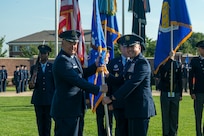 U.S. Air force Col. hands guidon to another Col. in front of The U.S. Air and Space Force Honor Guard.
