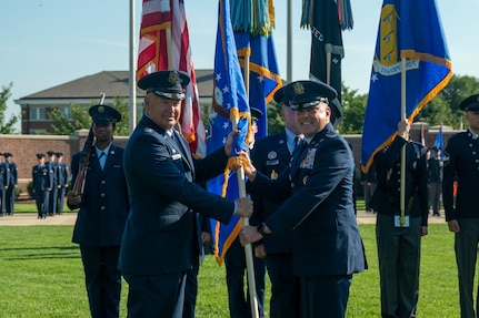 U.S. Air force Col. hands guidon to another Col. in front of The U.S. Air and Space Force Honor Guard.