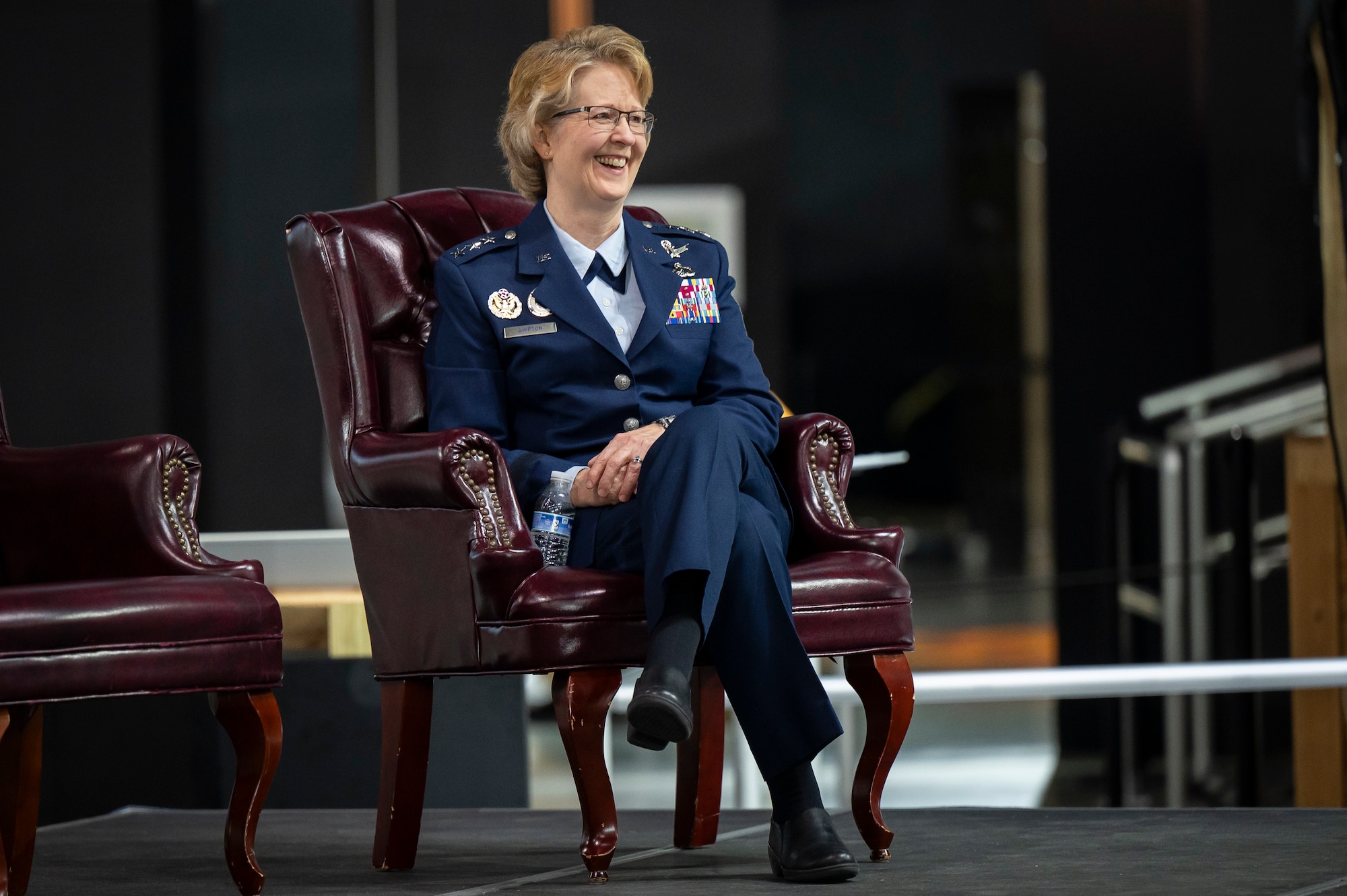 Female Air Force officer wearing dress blues sits in chair on stage.