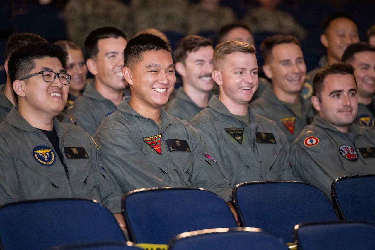 Dozens of men in flights suits laugh while sitting in an auditorium.