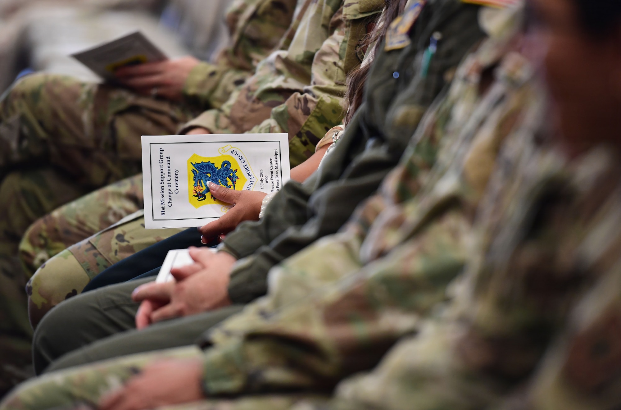 A person in a line of people sitting in chairs holds an event program.