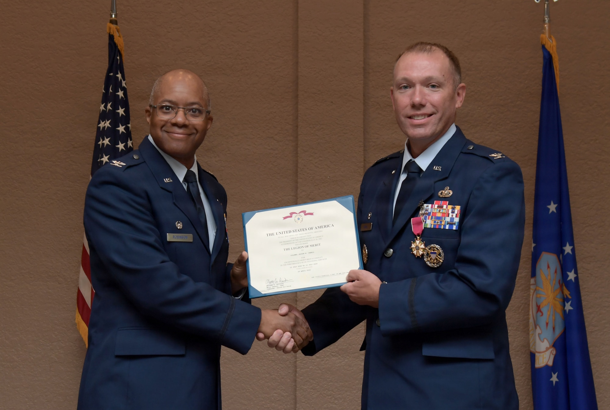 Two men in U.S. Air Force uniforms hold a certificate while posing for the camera.