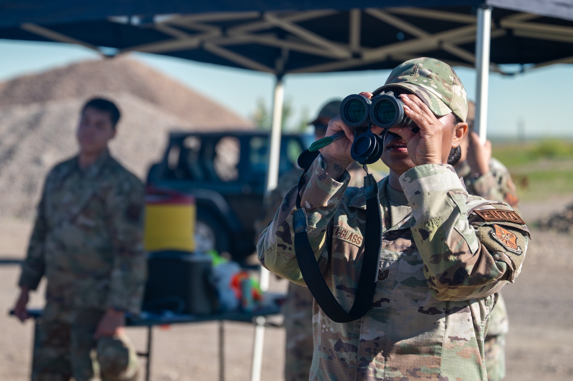 A uniformed woman looks through binoculars.